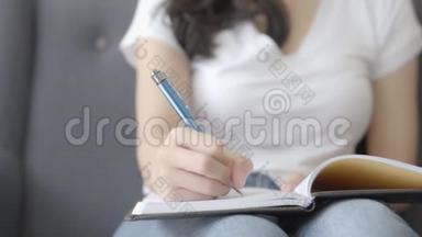 特写亚洲女人放松，躺在沙发上写书，写日记在家里的沙发上